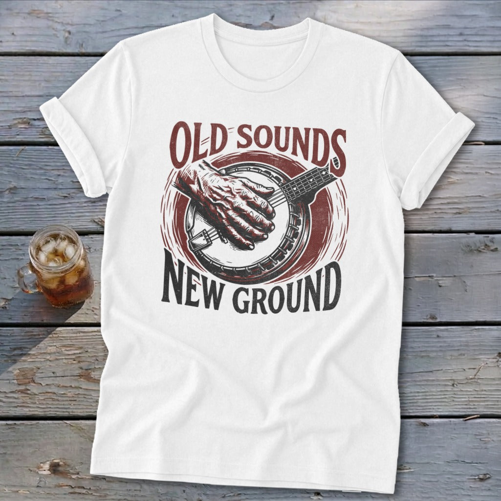 A white t-shirt features a graphic print of a hand playing a banjo and text that reads Old Sounds New Ground.