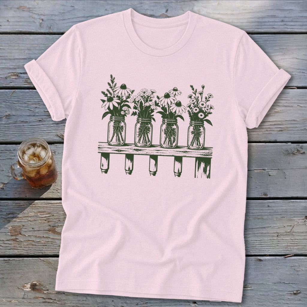 Light pink short-sleeve t-shirt featuring a green graphic of four mason jars filled with wildflowers resting on a wooden shelf.