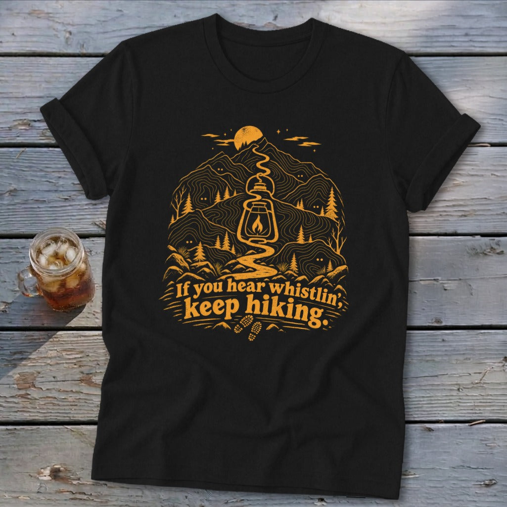 Black t-shirt with orange graphic of lantern, mountains, trees, and text "If you hear whistlin', keep hiking."