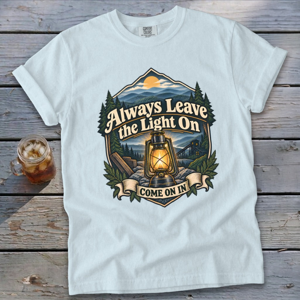 Light blue t-shirt with a graphic of a lantern and text "Always Leave the Light On Come on In".