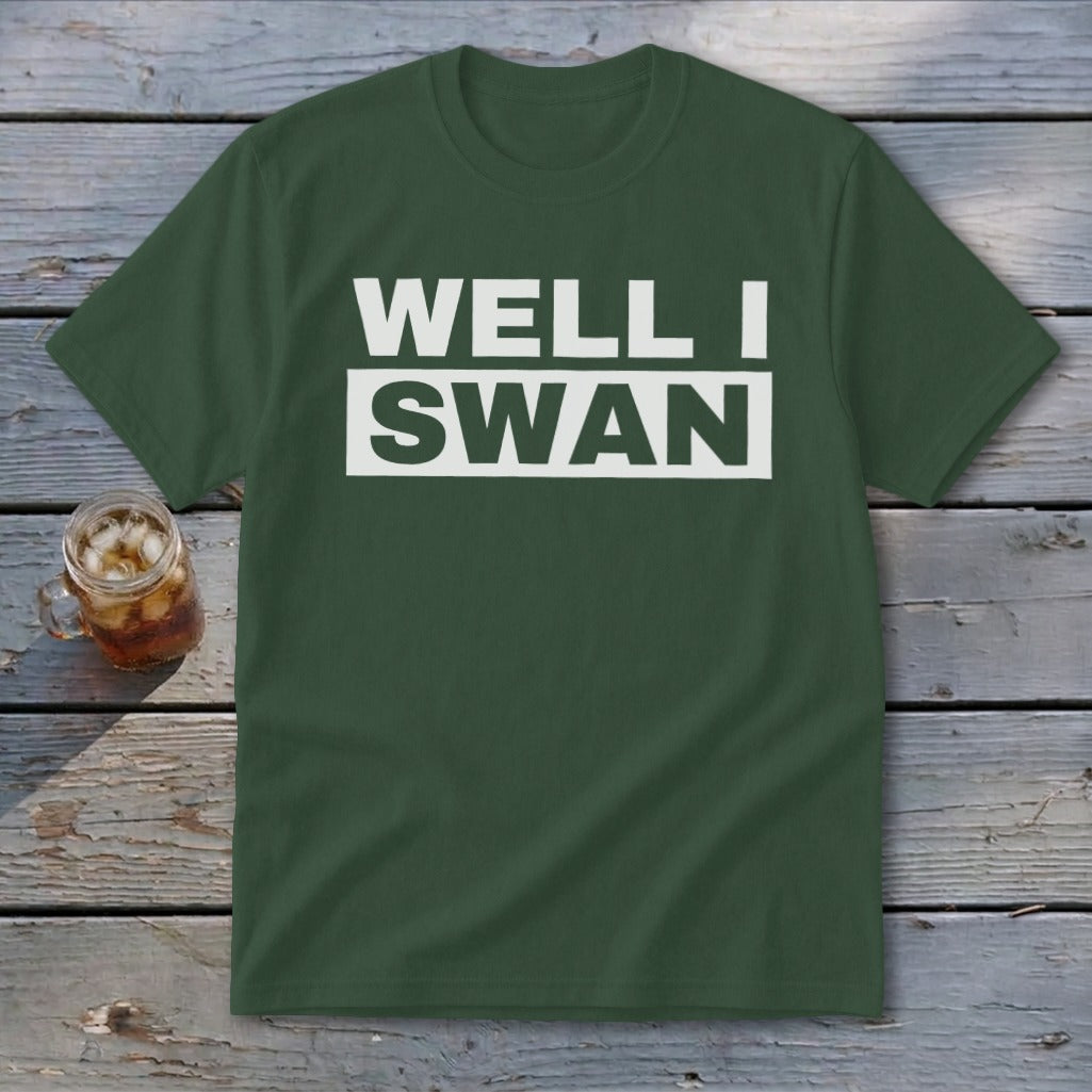 Dark green crewneck t-shirt featuring the white text WELL I SWAN lying on a wooden surface.
