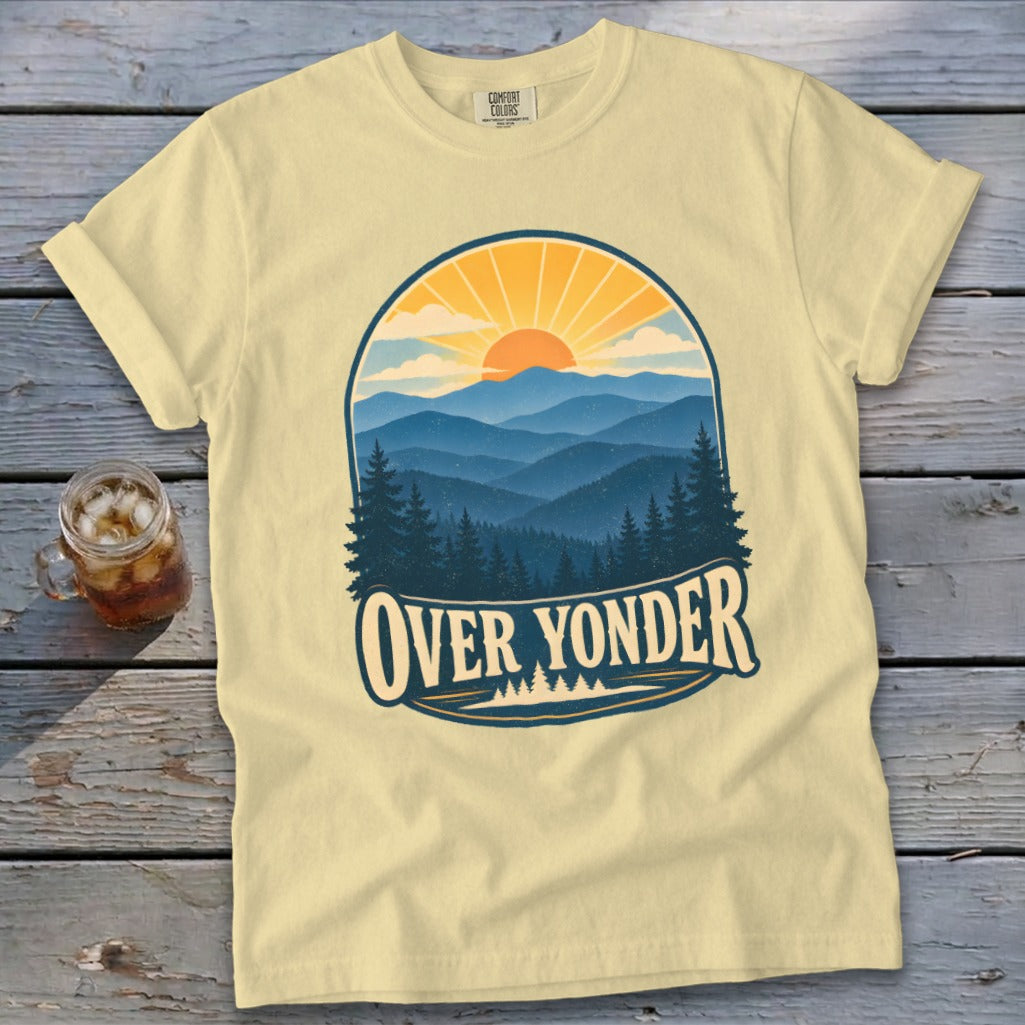 A cream-colored t-shirt with a vintage graphic of layered blue mountains, pine trees, and a setting sun.