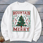 A white crewneck sweatshirt features a green-bordered graphic with a Christmas tree and the text Mountain Merry.