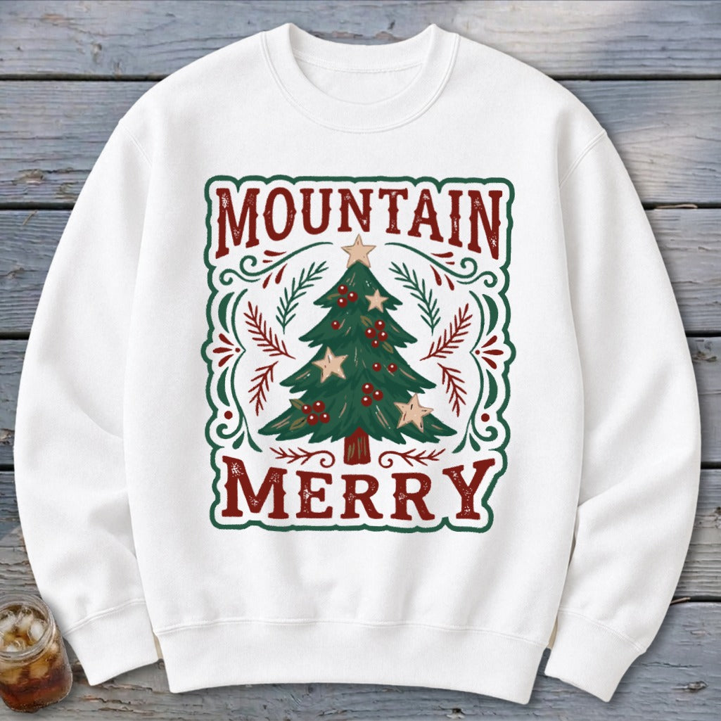 A white crewneck sweatshirt features a green-bordered graphic with a Christmas tree and the text Mountain Merry.