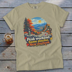 Tan t-shirt with "Peak weekend. Same playlist. New overlook." text and mountain scenery graphic.