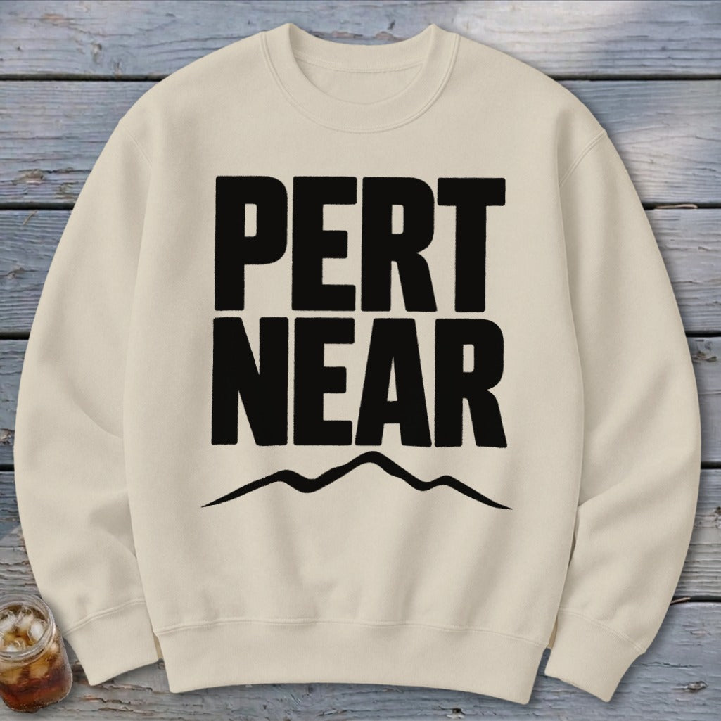 A cream-colored crewneck sweatshirt featuring large black bold text reading PERT NEAR above a mountain outline.