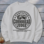 A white crewneck sweatshirt features a black circular graphic with text reading Certified Cornbread Judge.