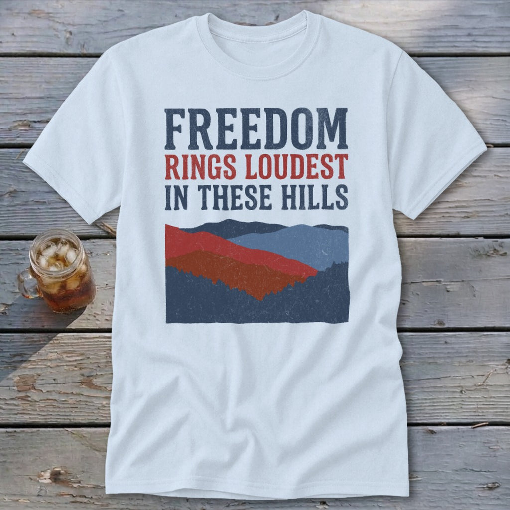 A white t-shirt featuring the text "FREEDOM RINGS LOUDEST IN THESE HILLS" above a mountain graphic.