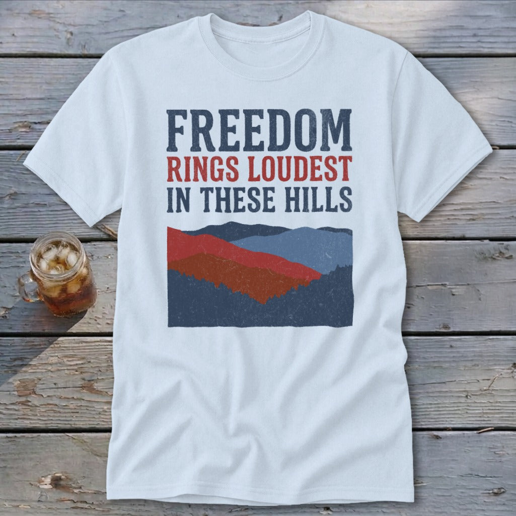 A white t-shirt featuring the text "FREEDOM RINGS LOUDEST IN THESE HILLS" above a mountain graphic.