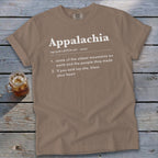 Brown t-shirt featuring dictionary-style text defining Appalachia, laid flat on a rustic wooden surface next to a glass of iced tea.
